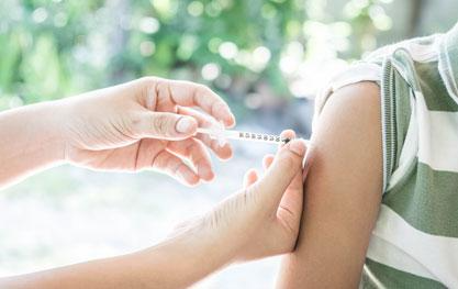 Close-up of a healthcare professional administering an injection into a person’s upper arm, with a soft outdoor background and natural lighting.