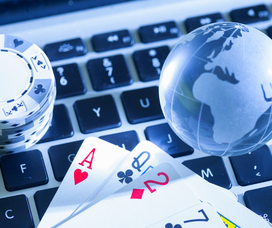 Playing cards and poker chips placed on a computer keyboard beside a small globe, suggesting online gambling, digital gaming, or global online betting activity.