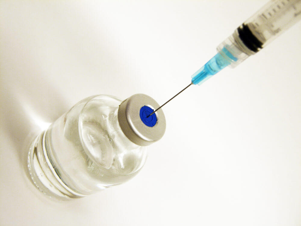 Close-up of a syringe needle inserted into a medical vial, representing medication or vaccine preparation in a healthcare setting.