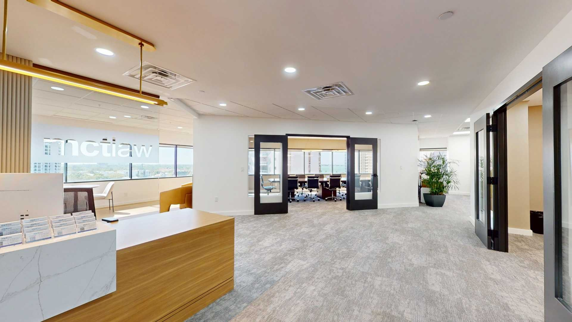 Front entrance area of mctlaw's Sarasota office featuring a reception desk, glass-walled break room, and large windows with a city view.