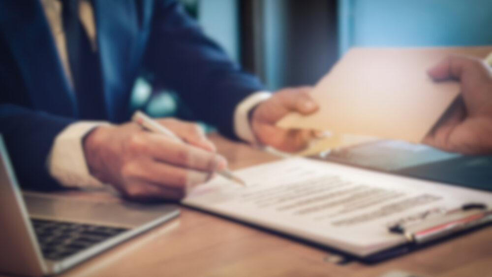 A man signs a document while another person observes, indicating a formal agreement or transaction.
