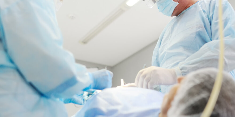 A surgeon in scrubs performs surgery on a patient lying on an operating table in a sterile environment.