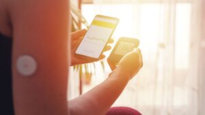 Medical whistleblowers flipbox homepage Person with a glucose sensor on their upper arm reviewing blood sugar readings on a smartphone and handheld monitor